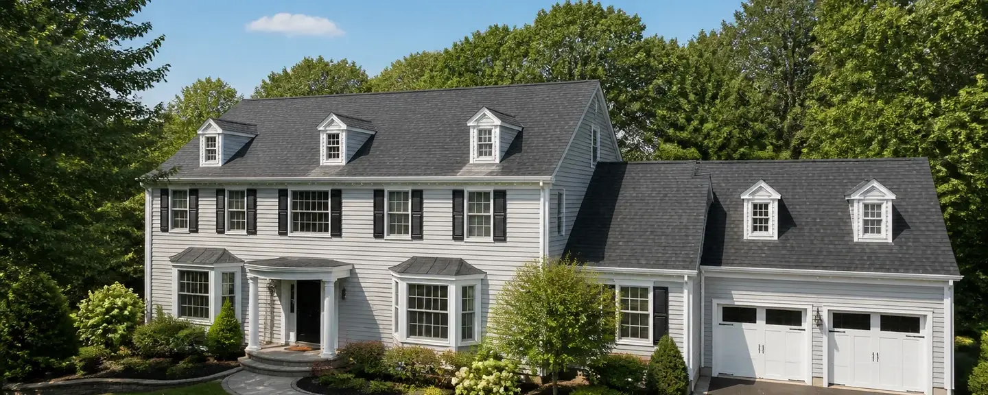 Two-story center-hall colonial with a charcoal architectural shingle roof, dormers, and an attached garage on a wooded lot.