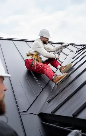 Roofer in a hard hat working on a standing-seam metal roof.
