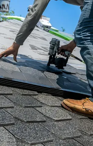 Close-up of hands installing asphalt shingles with a pneumatic nail gun.