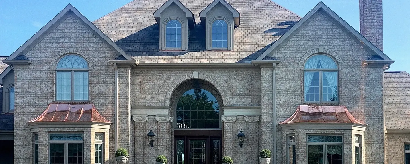 Completed dark gray architectural asphalt shingle roof on a large brick home with dormers, copper bay window roofs, and a brick chimney.