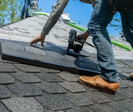 Close-up of hands installing asphalt shingles with a pneumatic nail gun.