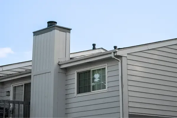 House exterior with grey siding, chimney, and window under a clear sky.