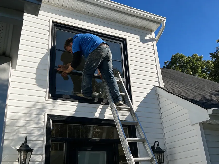 Contractor on a ladder installing a window from outside the house.