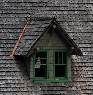 Renovated green dormer with new shingles after restoration.